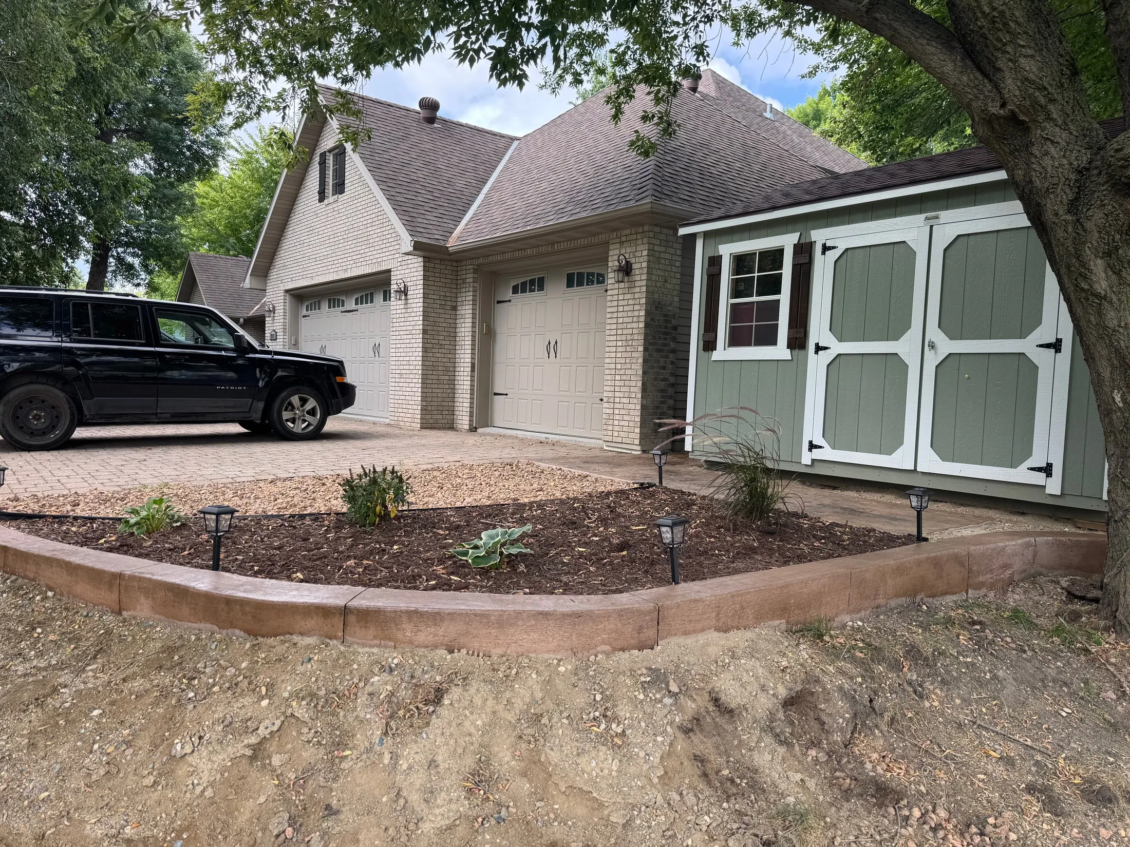 Curved edging and planting beds beside a home and shed.