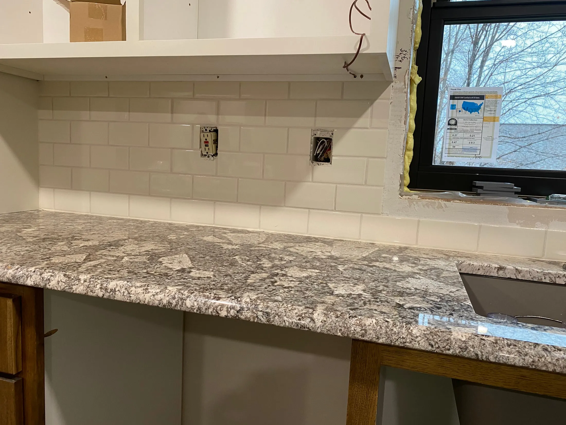 White subway tile kitchen backsplash over granite counters, mid-installation.