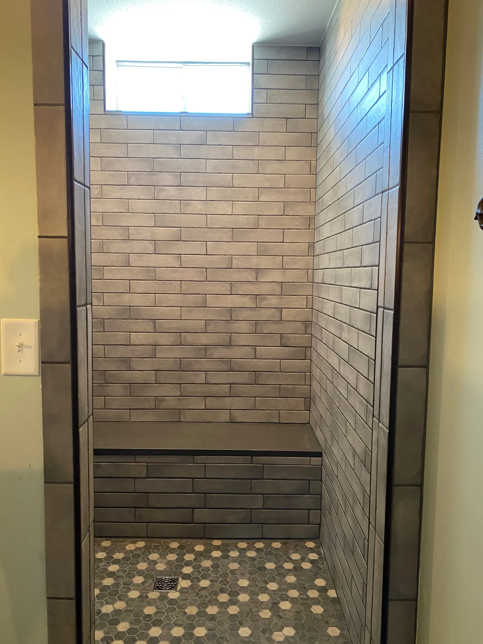 Walk-in shower with gray tile, window and built-in bench.