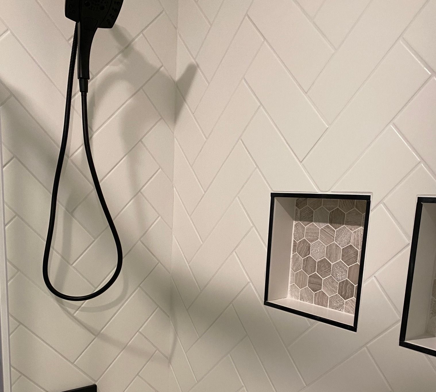 White herringbone shower tile with black-trimmed hexagon tile niches