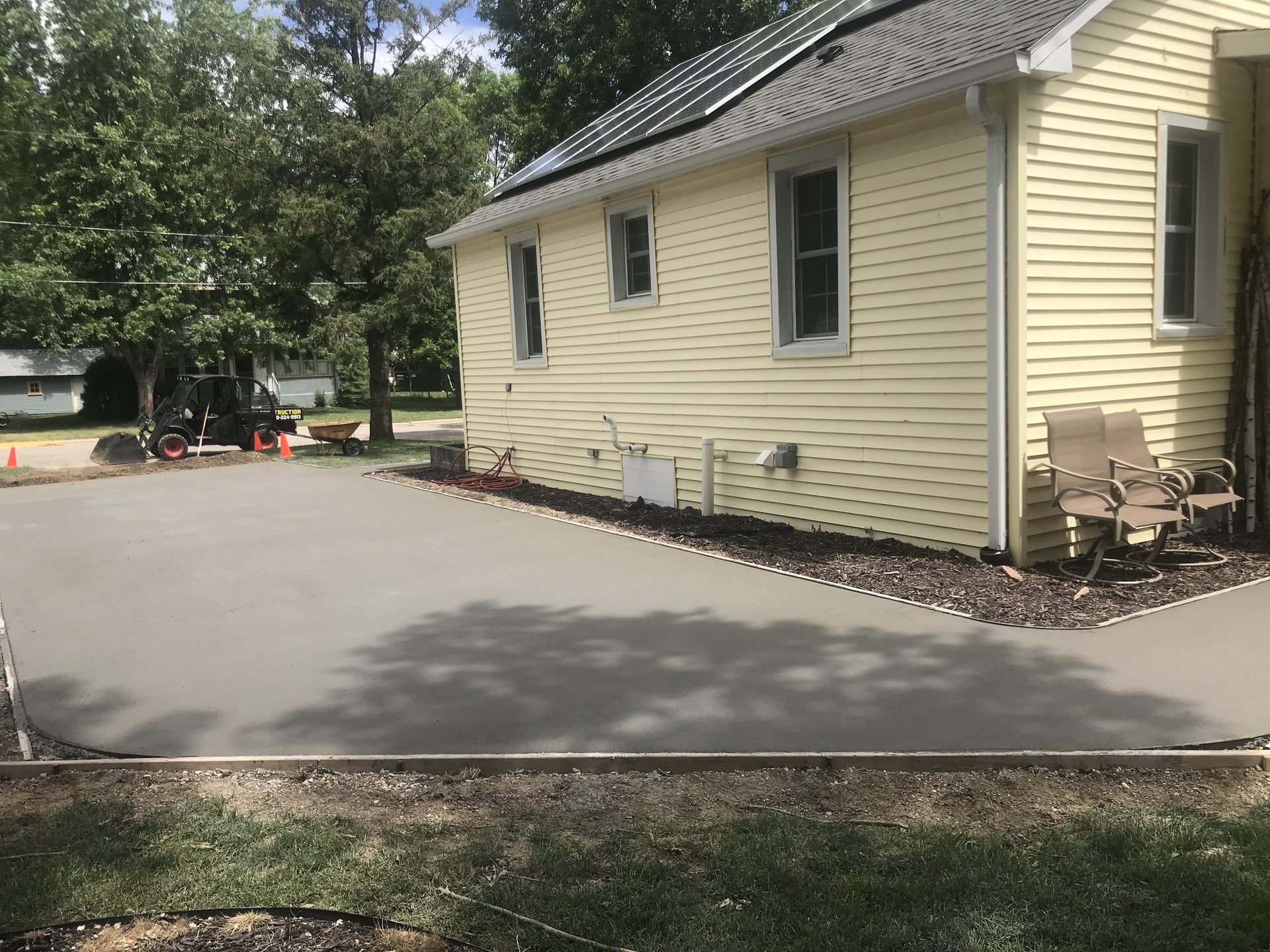 Newly installed concrete driveway leading to cream-colored house with dark roof and landscaped foundation.
