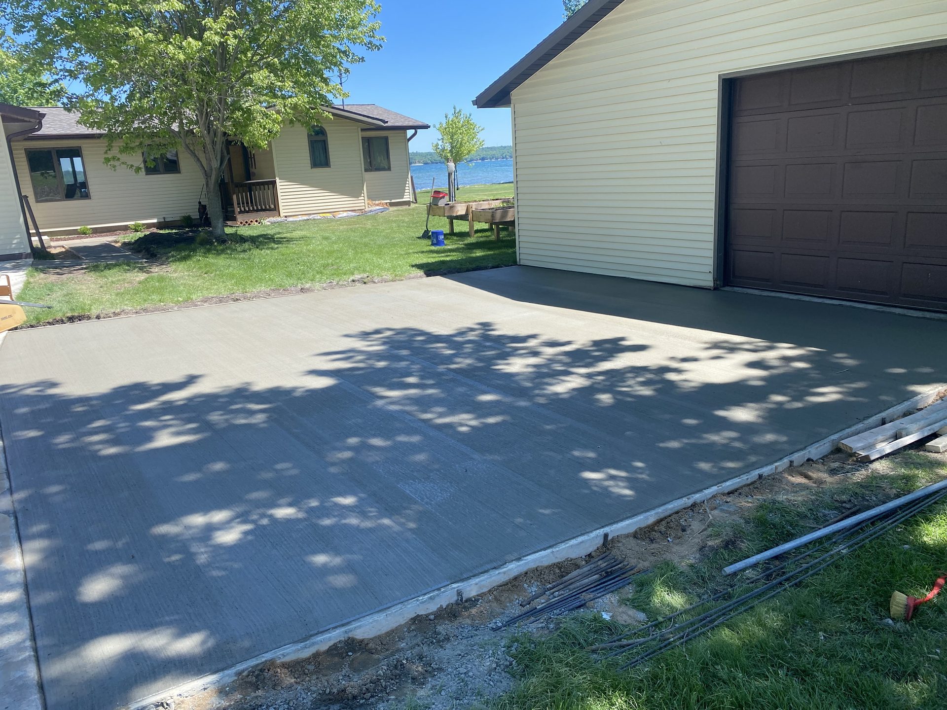 Finished concrete driveway alongside a garage and residential home with water view in background.