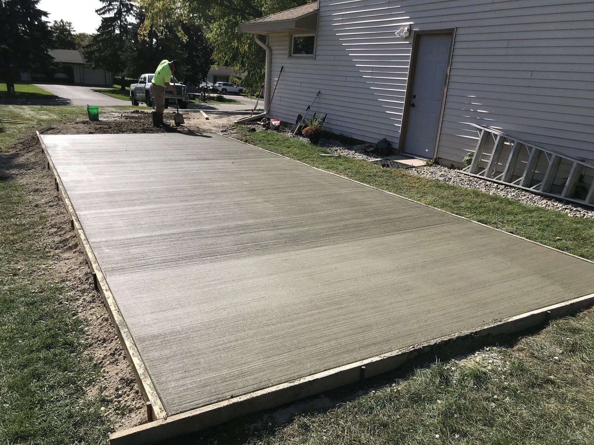 Newly poured and finished concrete pad adjacent to residential home, ready for use as foundation or driveway base.
