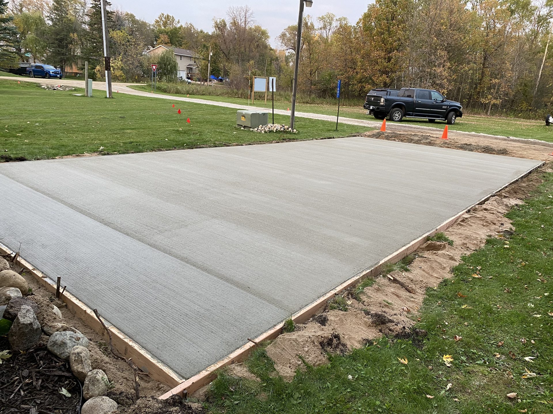 Newly finished concrete pad in residential setting with grass, trees, and utility poles in background.