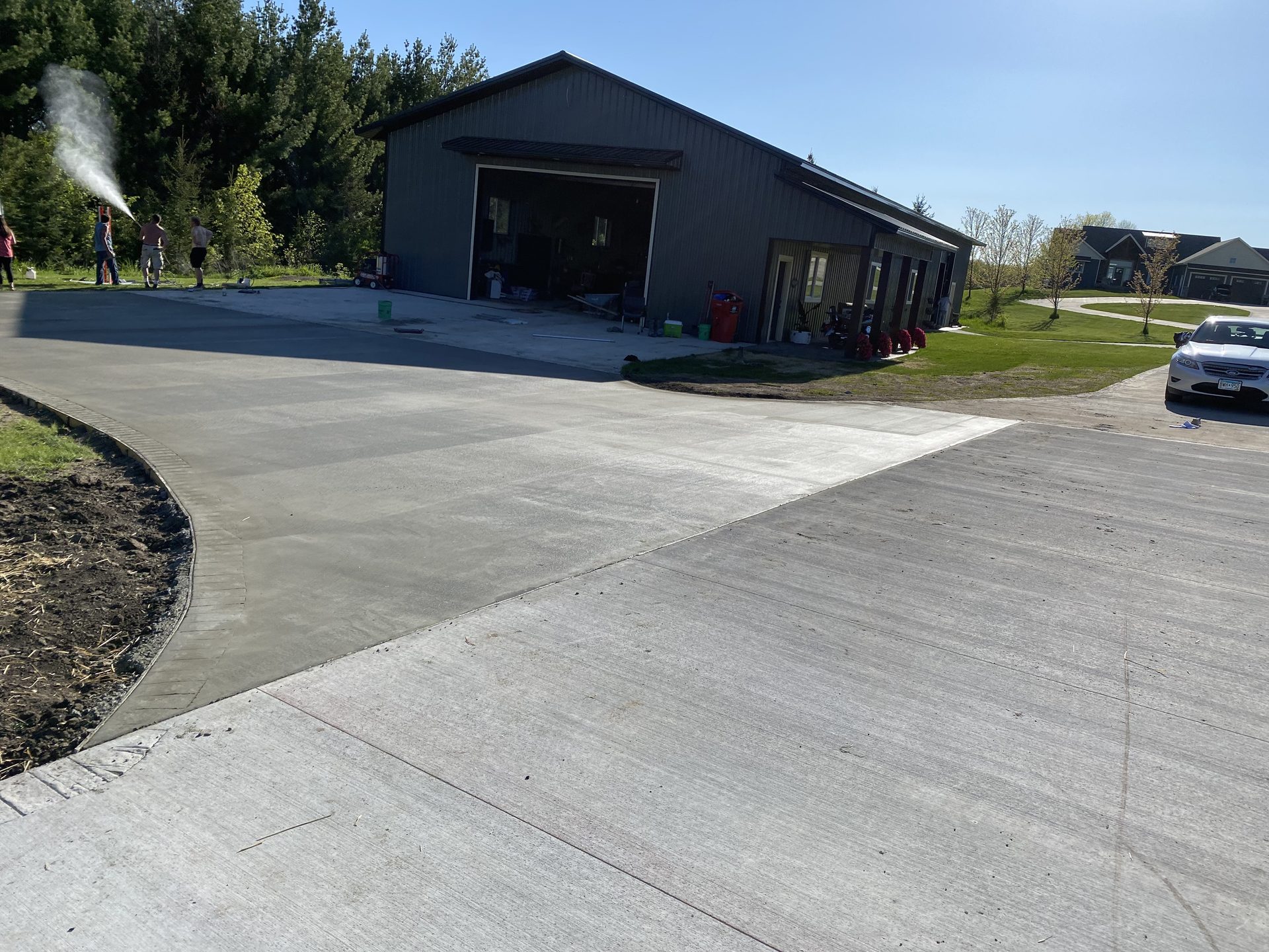 Newly poured concrete driveway and apron in front of modern black metal building with attached residential spaces.