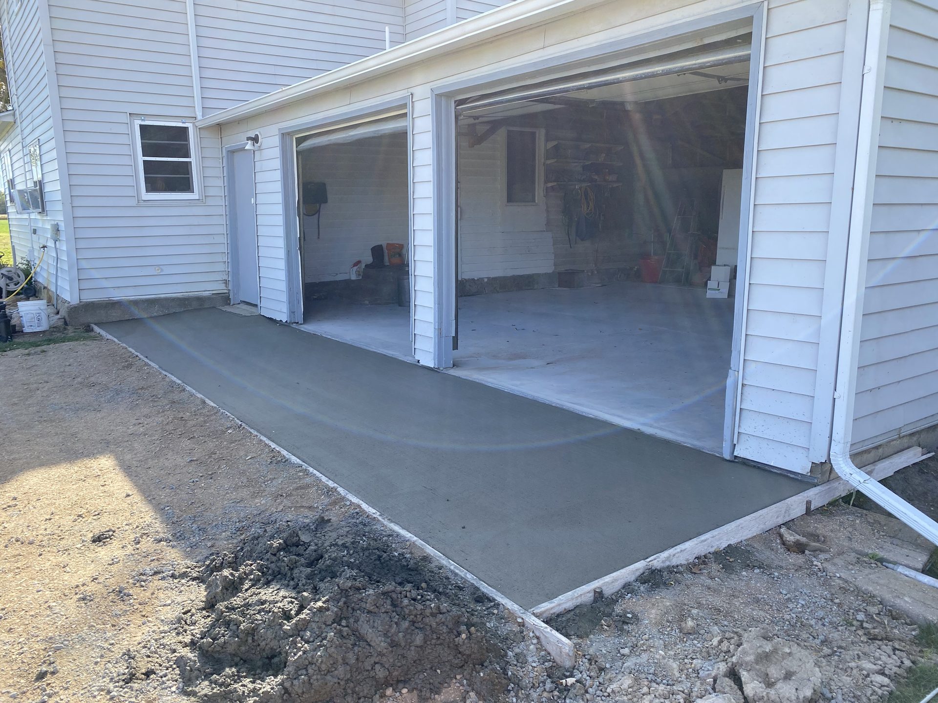 Newly poured concrete driveway adjacent to white vinyl-sided home with glass sliding doors.