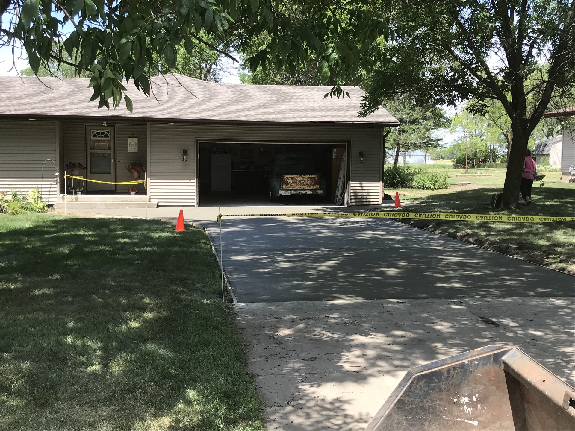 New asphalt concrete driveway in progress with fresh seal coating applied, bordered by manicured lawn and mature trees.
