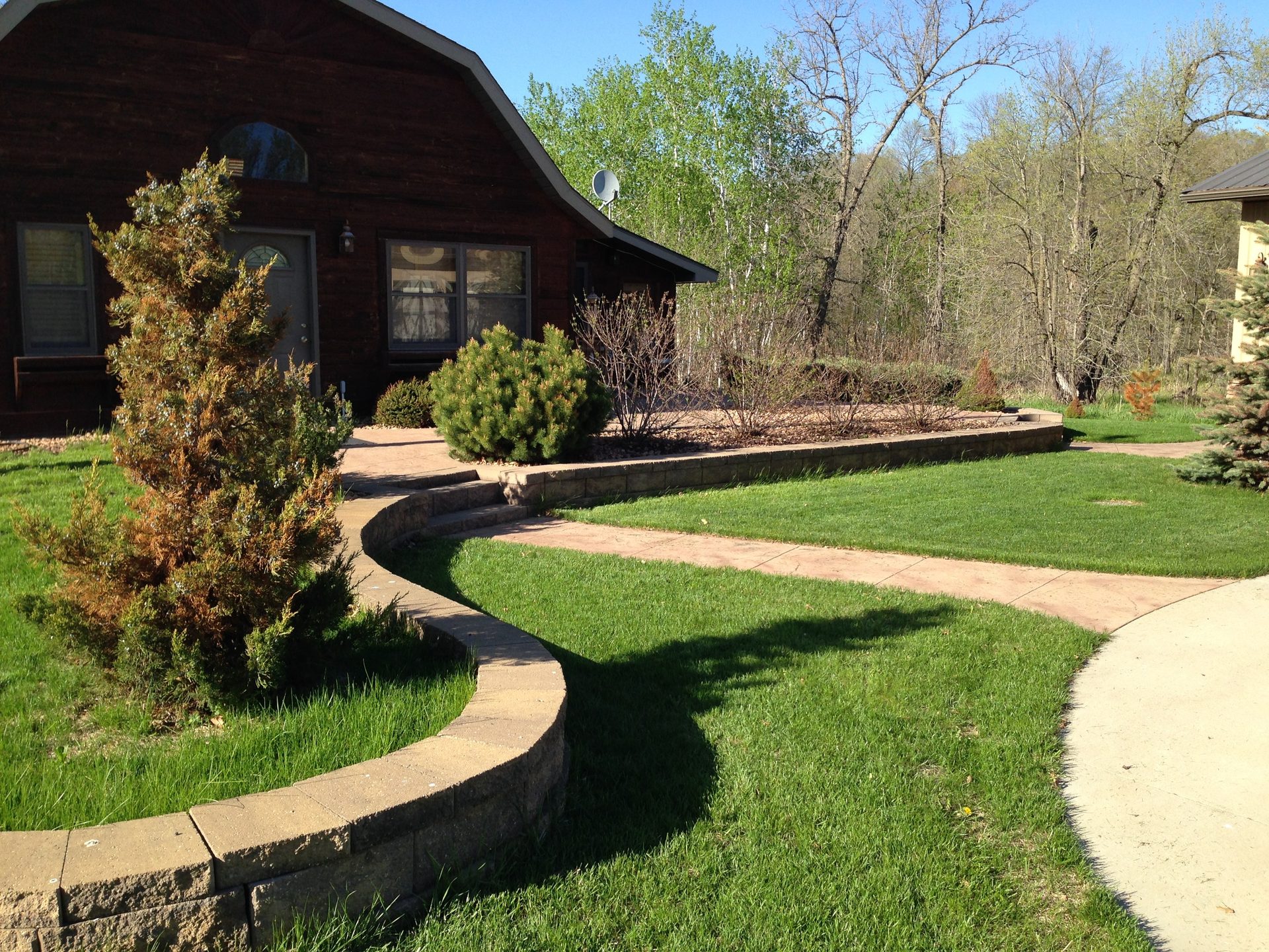Completed residential landscaping with curved concrete edging, lawn, and perennial beds bordering a dark timber-frame home.