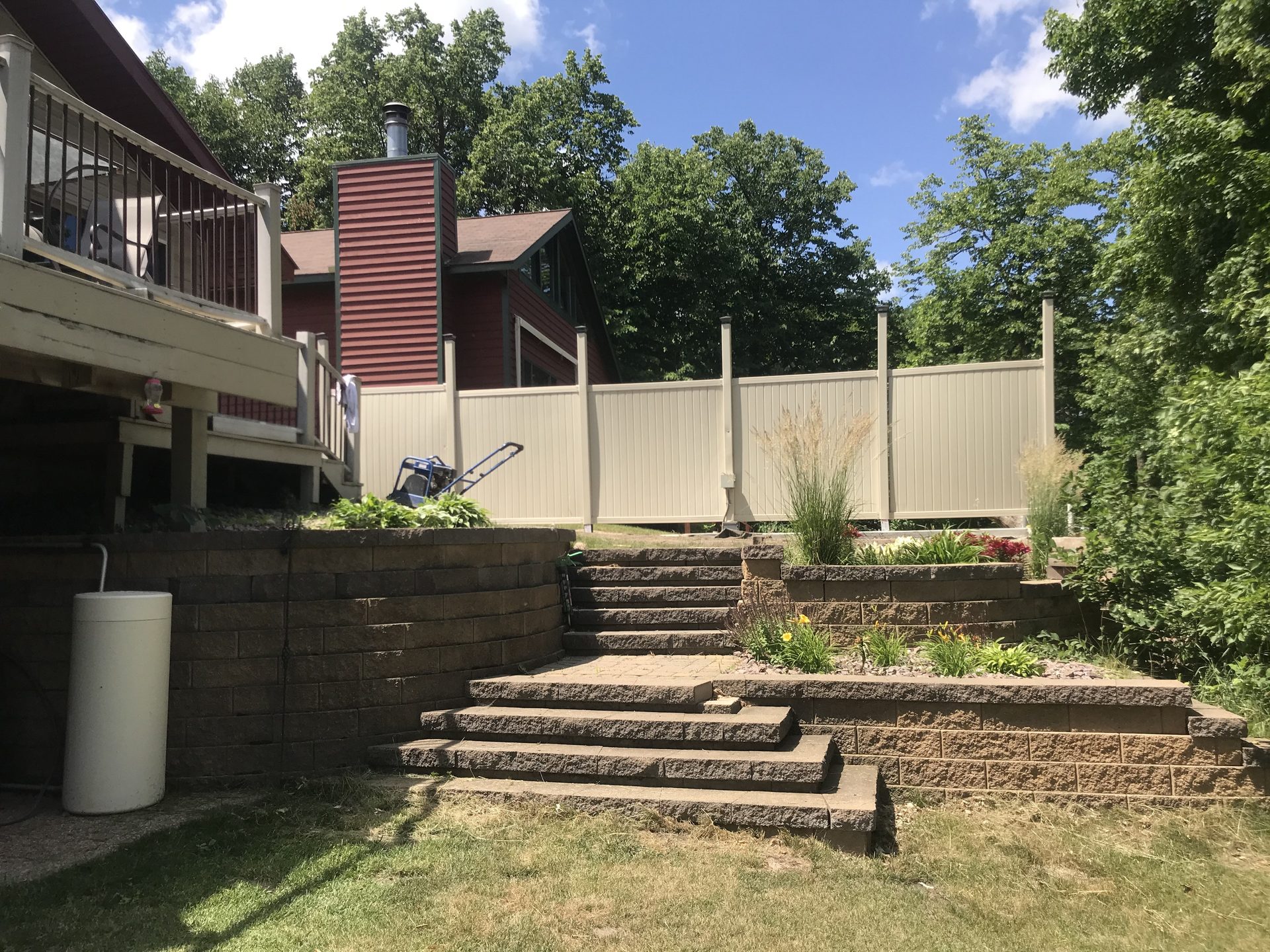 Tiered concrete retaining wall installation with integrated landscape planting beds and metal privacy fencing in background.
