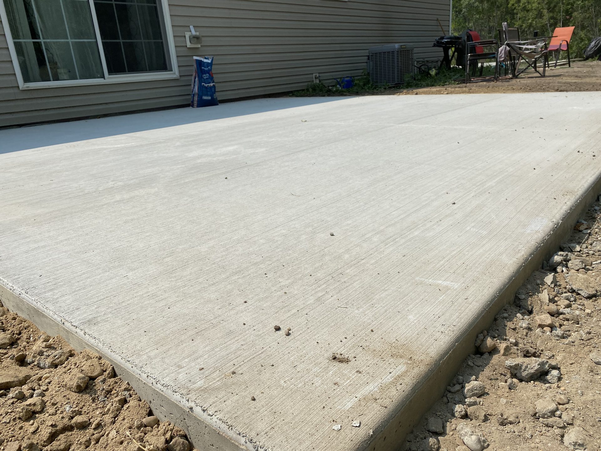 Newly poured concrete driveway pad alongside a residential home with gray siding, showing smooth finished surface and clean edges.