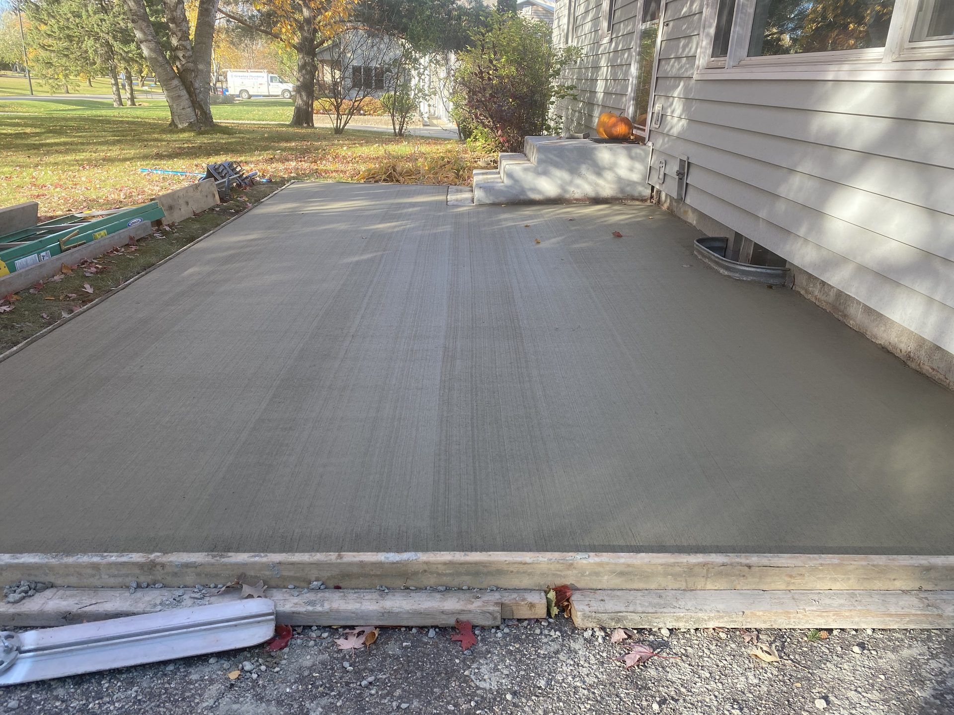 Newly finished concrete driveway with broom finish texture, adjoining a residential home with autumn foliage in background.