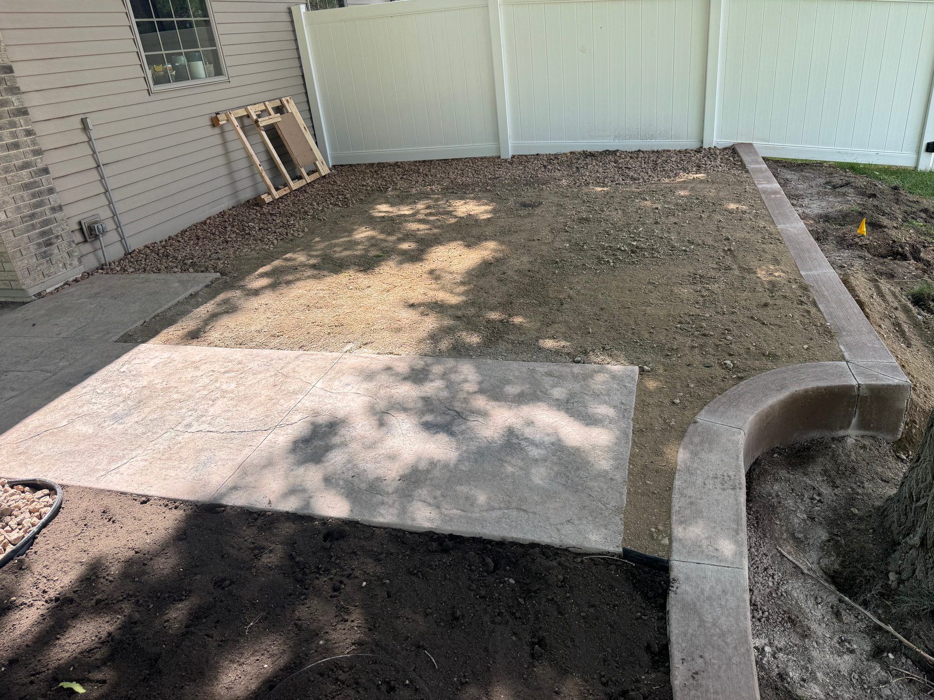 Stamped concrete patio with curved border, rock landscaping, and residential home in west-central Minnesota.