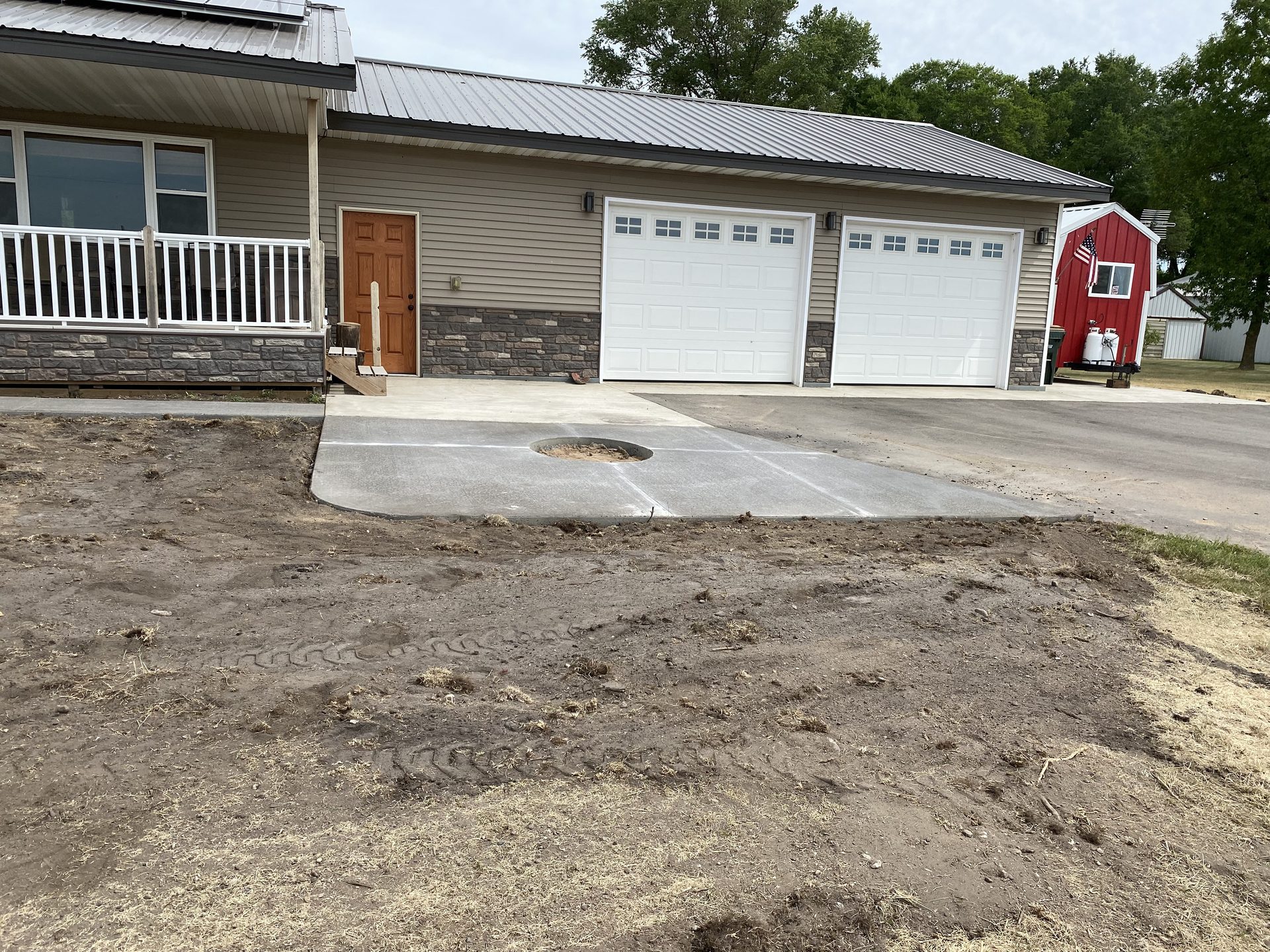 Finished concrete driveway with two garage doors adjacent to a residential home with metal roof and stone veneer base.