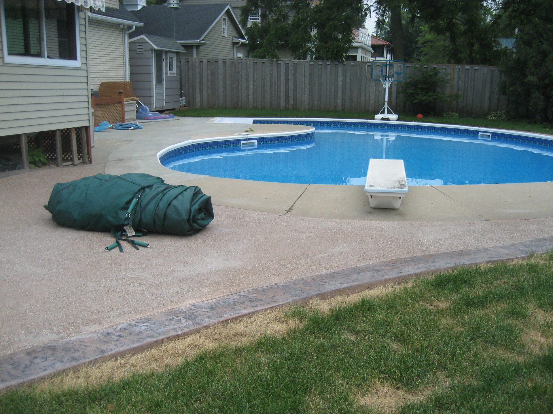 Completed in-ground swimming pool with blue interior and concrete deck surround, residential backyard setting.