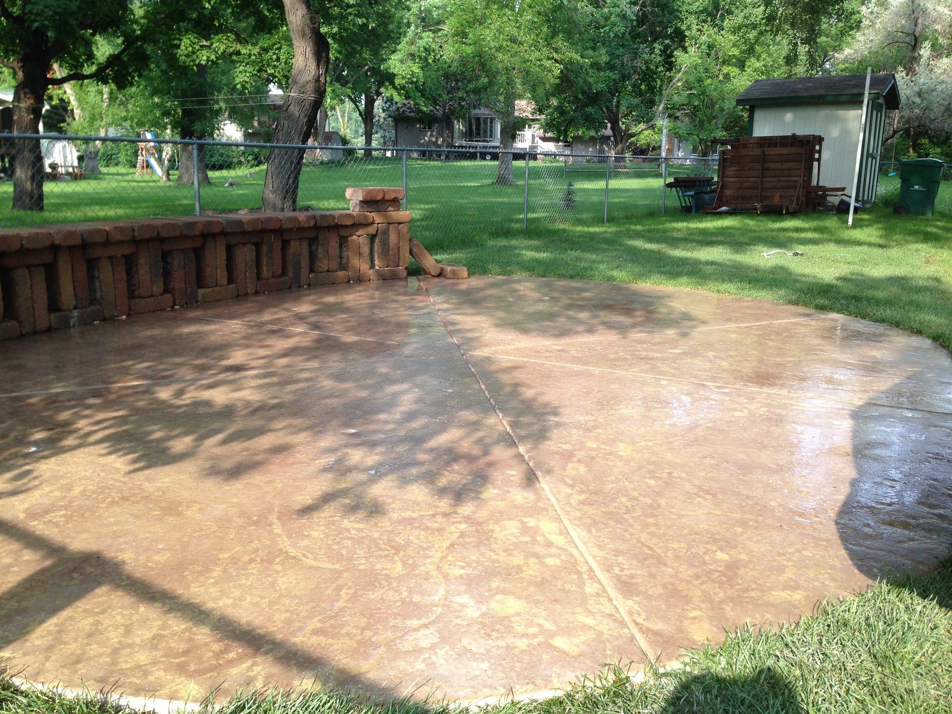 Finished concrete patio with brick border edging in residential backyard setting.
