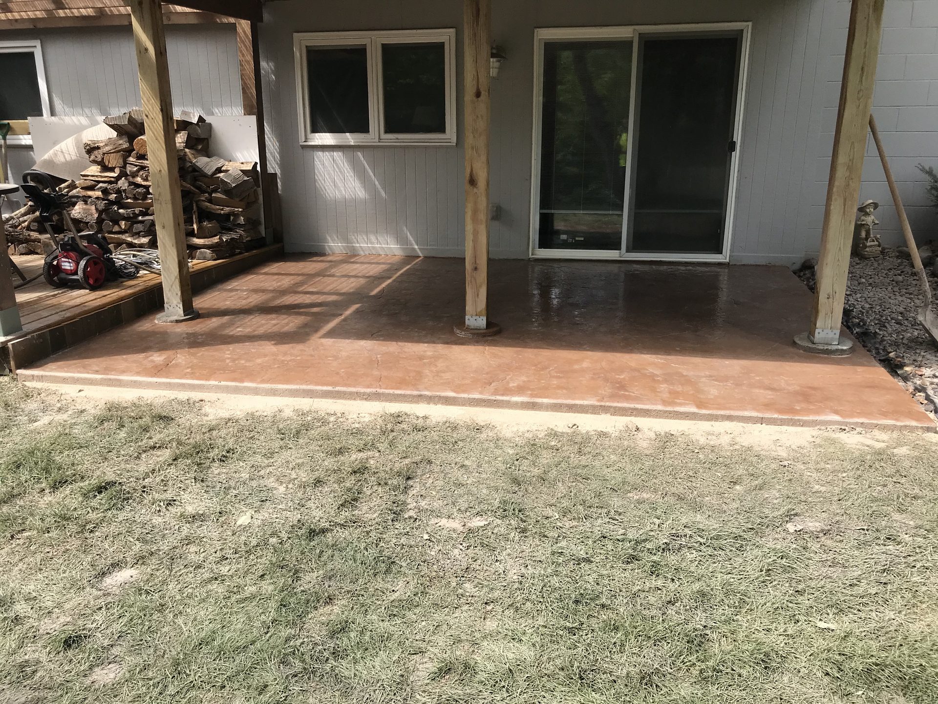 Finished concrete patio with wooden support posts adjacent to sliding glass doors and house exterior.