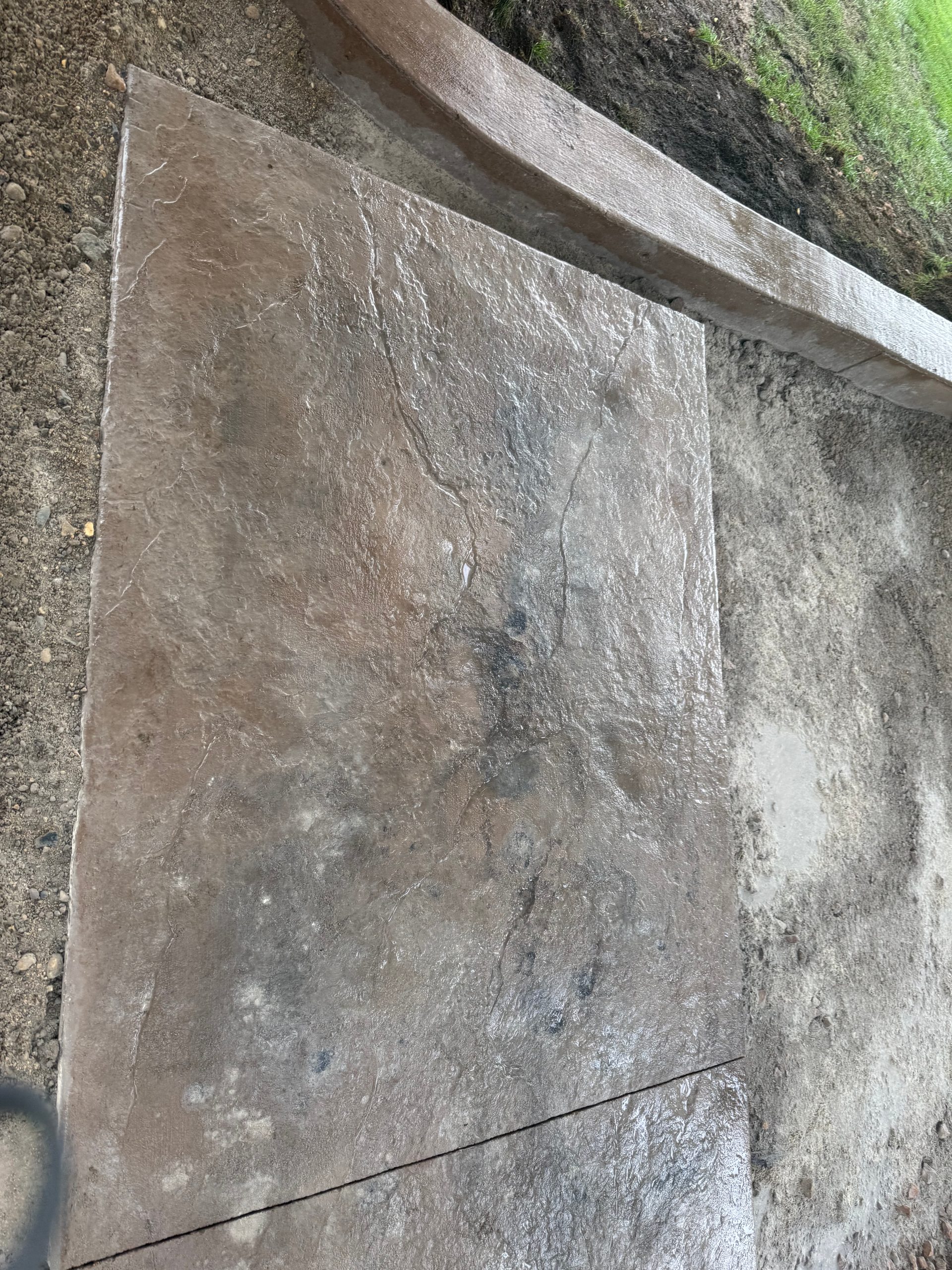 Stamped concrete patio corner with curved concrete border and surrounding soil prep in west-central Minnesota.