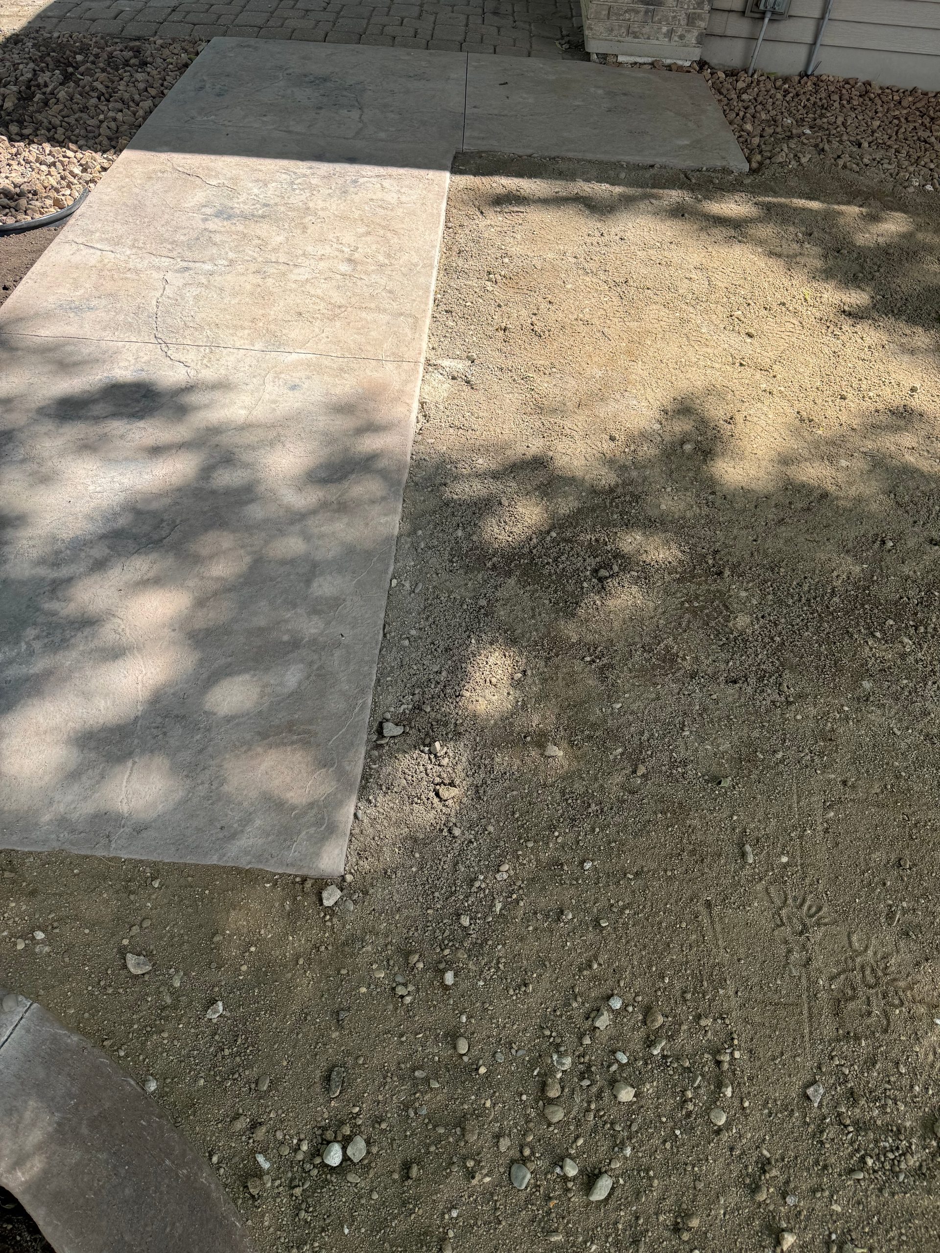 Newly poured stamped concrete patio with curved decorative border and fresh soil surround in west-central Minnesota.