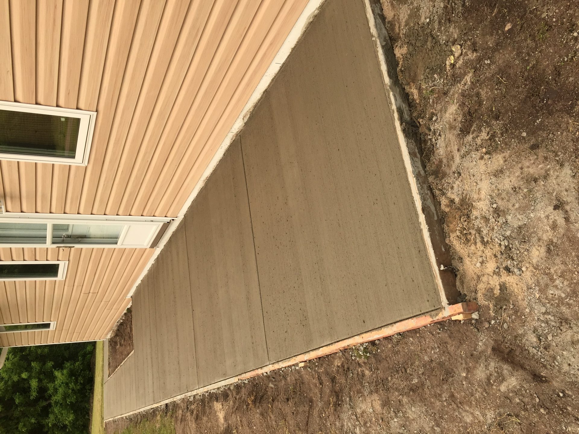 Finished concrete sidewalk alongside a metal-sided residential structure with white trim and windows.