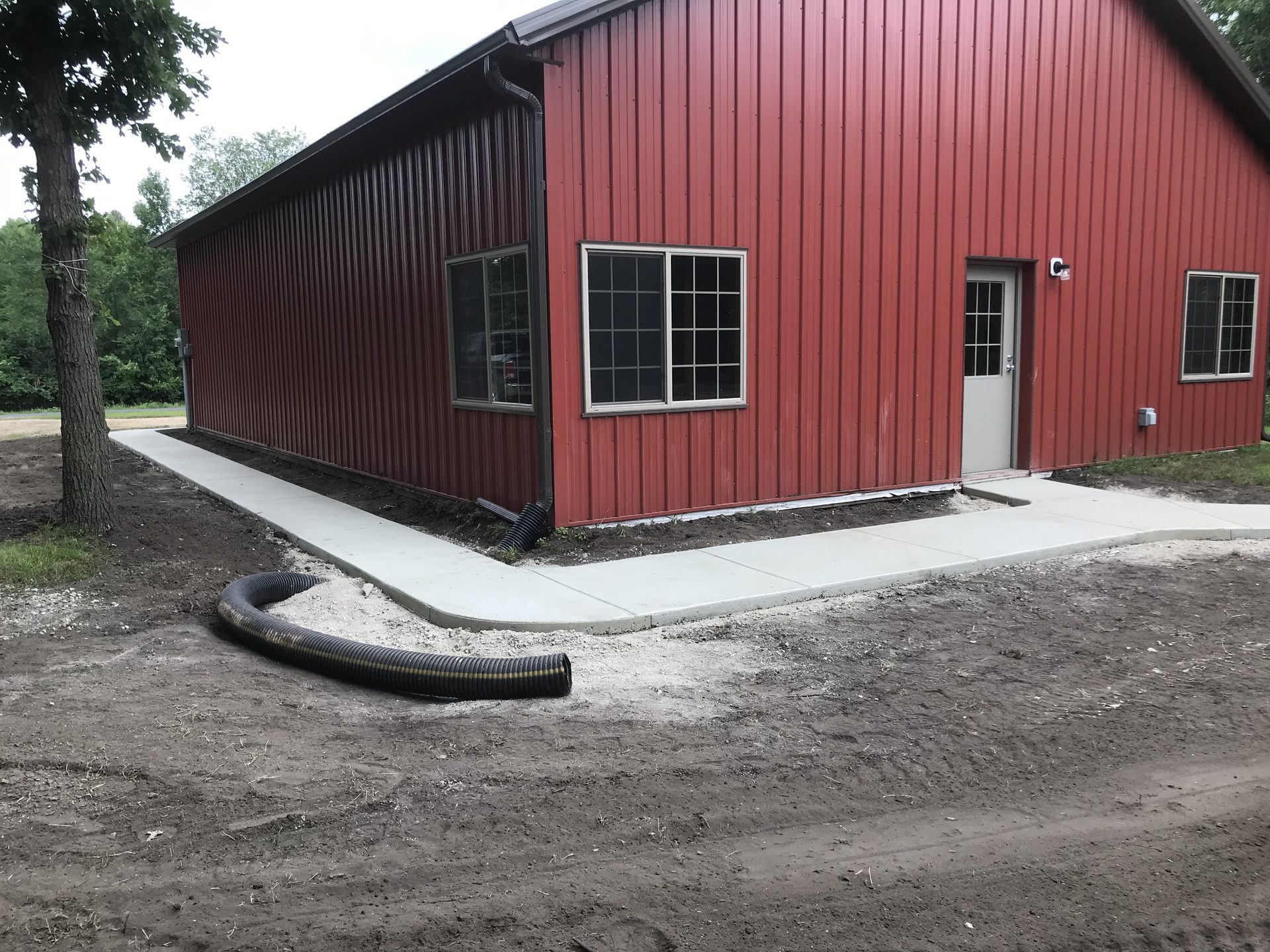 Completed red metal building with concrete foundation and sidewalk, featuring multiple windows and entry door.