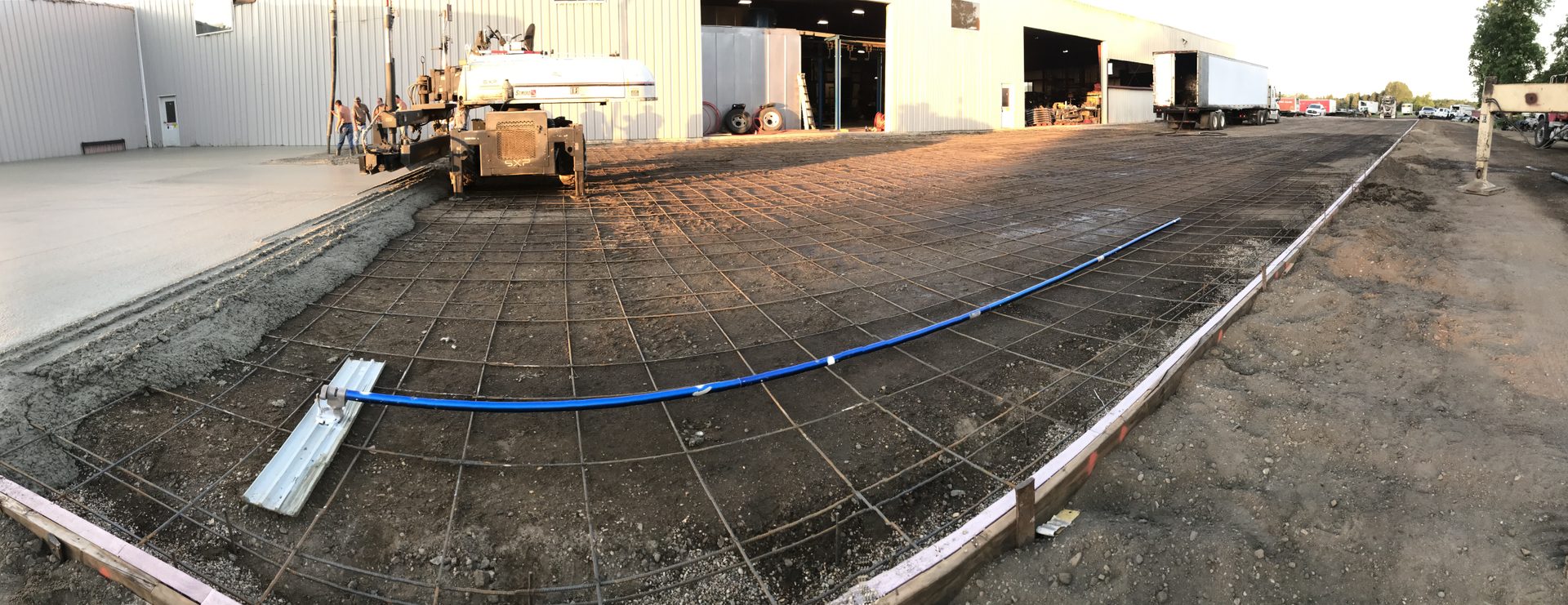 Concrete foundation with rebar grid laid out and blue conduit in place during active construction.