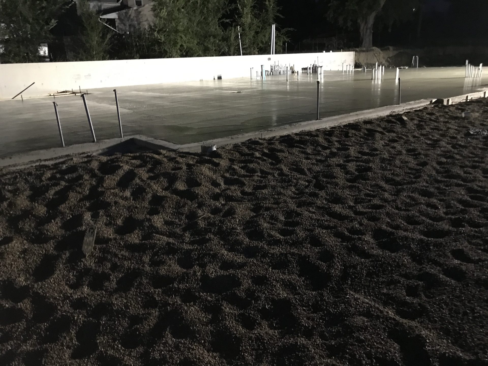 Concrete foundation pour in progress with metal stakes and forms visible, showing smooth gray concrete surface during curing phase.