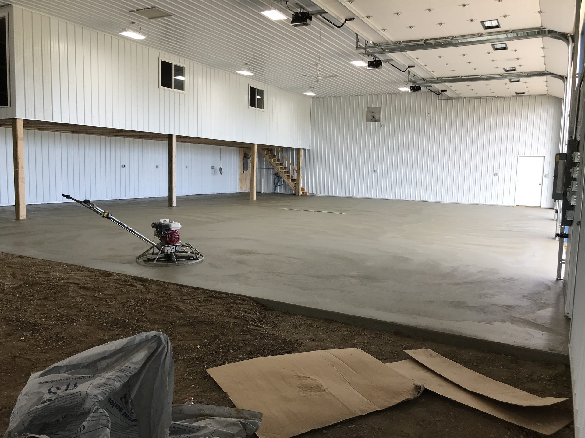Large concrete floor being finished in a bright agricultural or industrial building, with a power trowel visible on the fresh concrete surface.