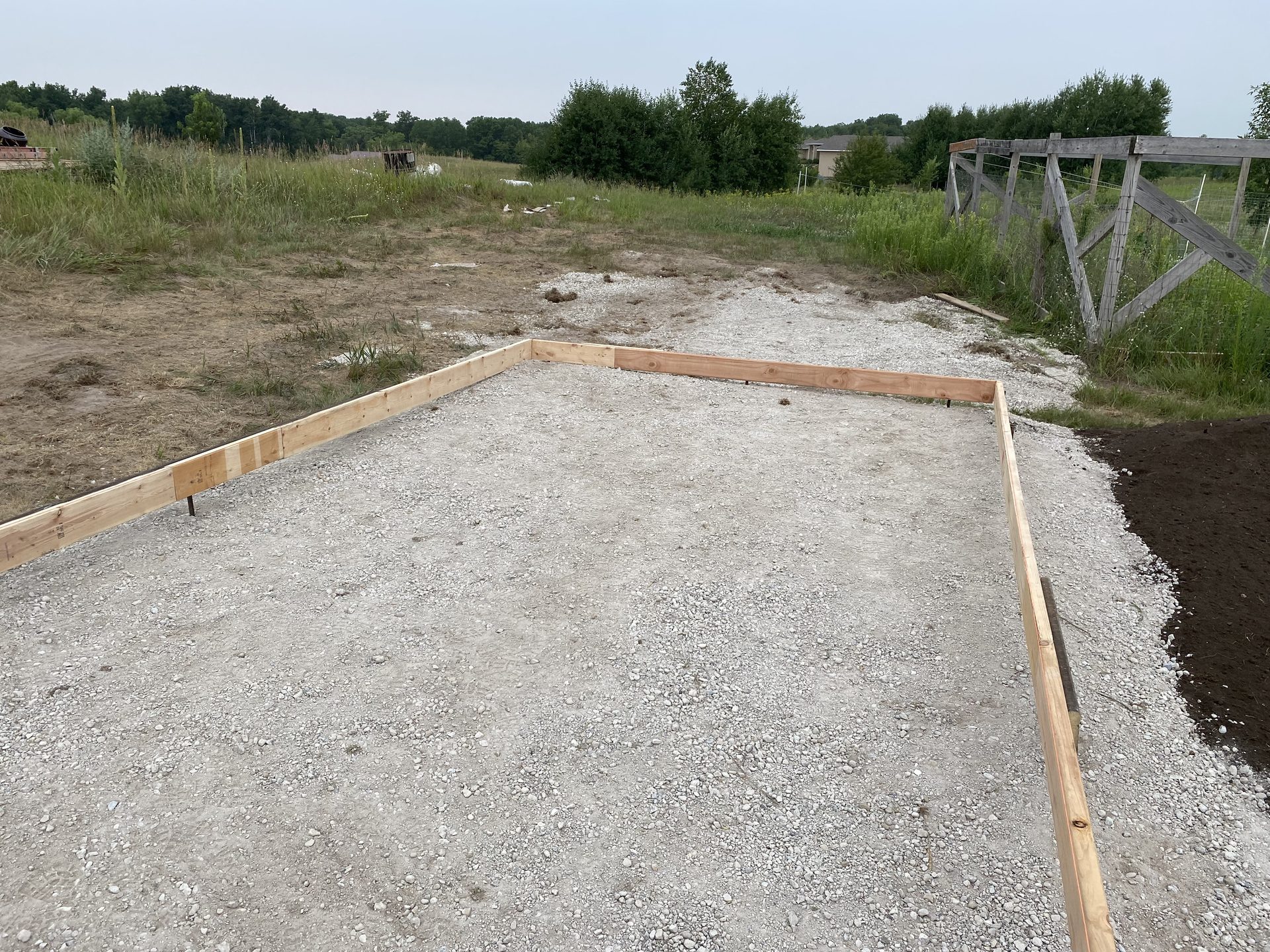 Concrete foundation base with wooden frame forms on rural jobsite during construction.