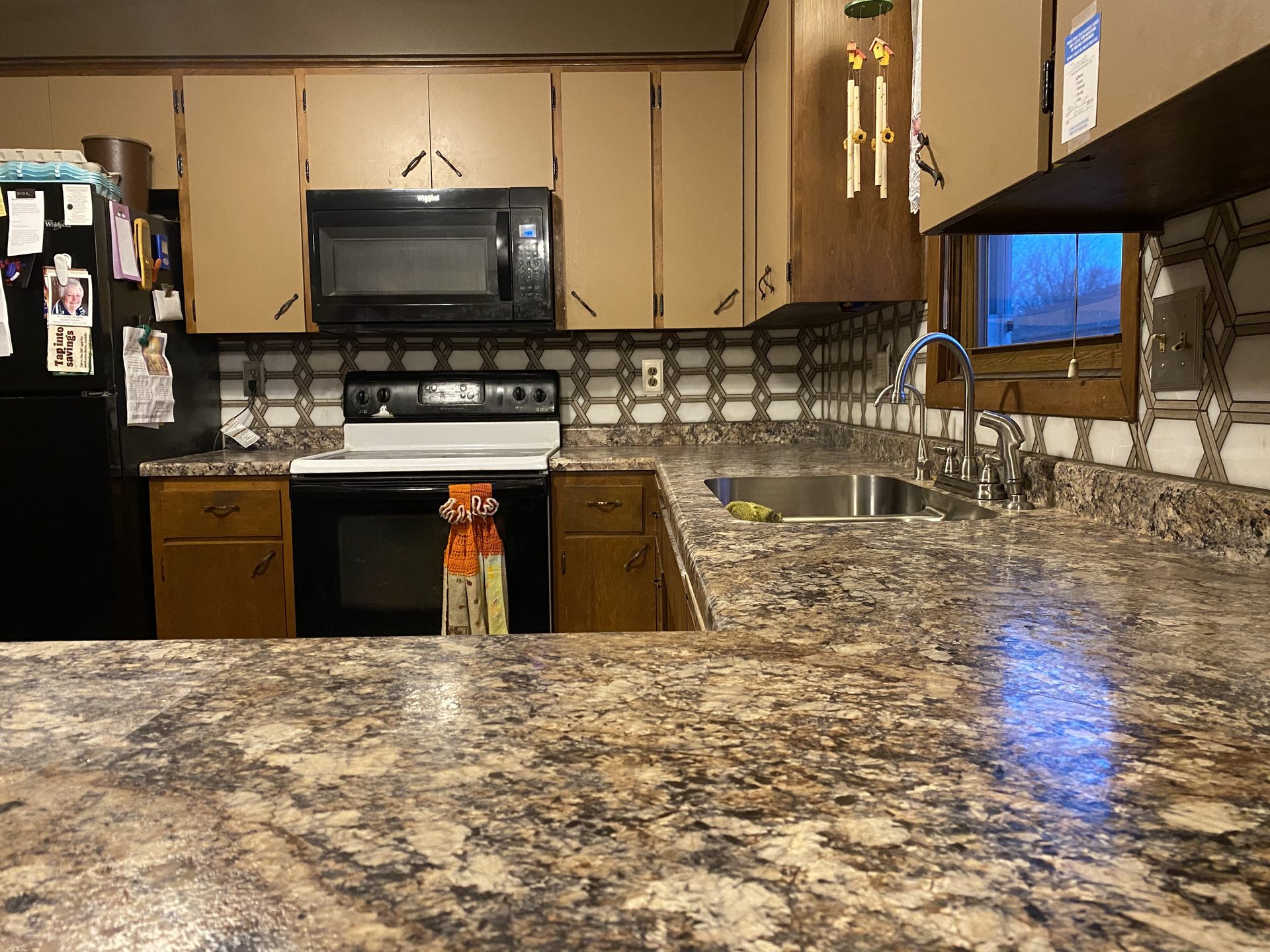 Finished kitchen renovation featuring granite countertops, geometric tile backsplash, stainless steel sink, and black appliances.
