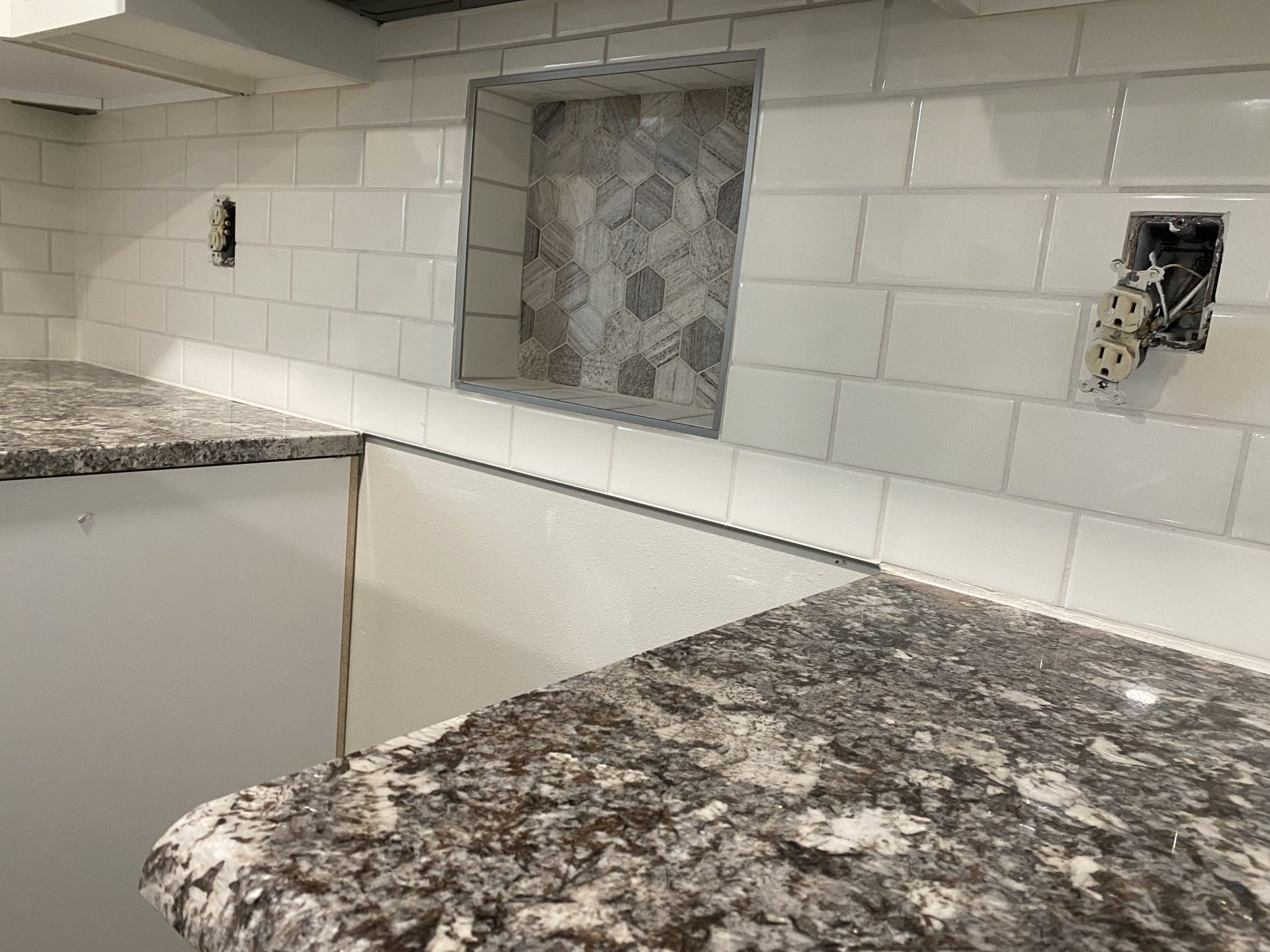 Completed kitchen backsplash featuring white subway tile with decorative hexagonal tile inset, paired with speckled gray countertops.