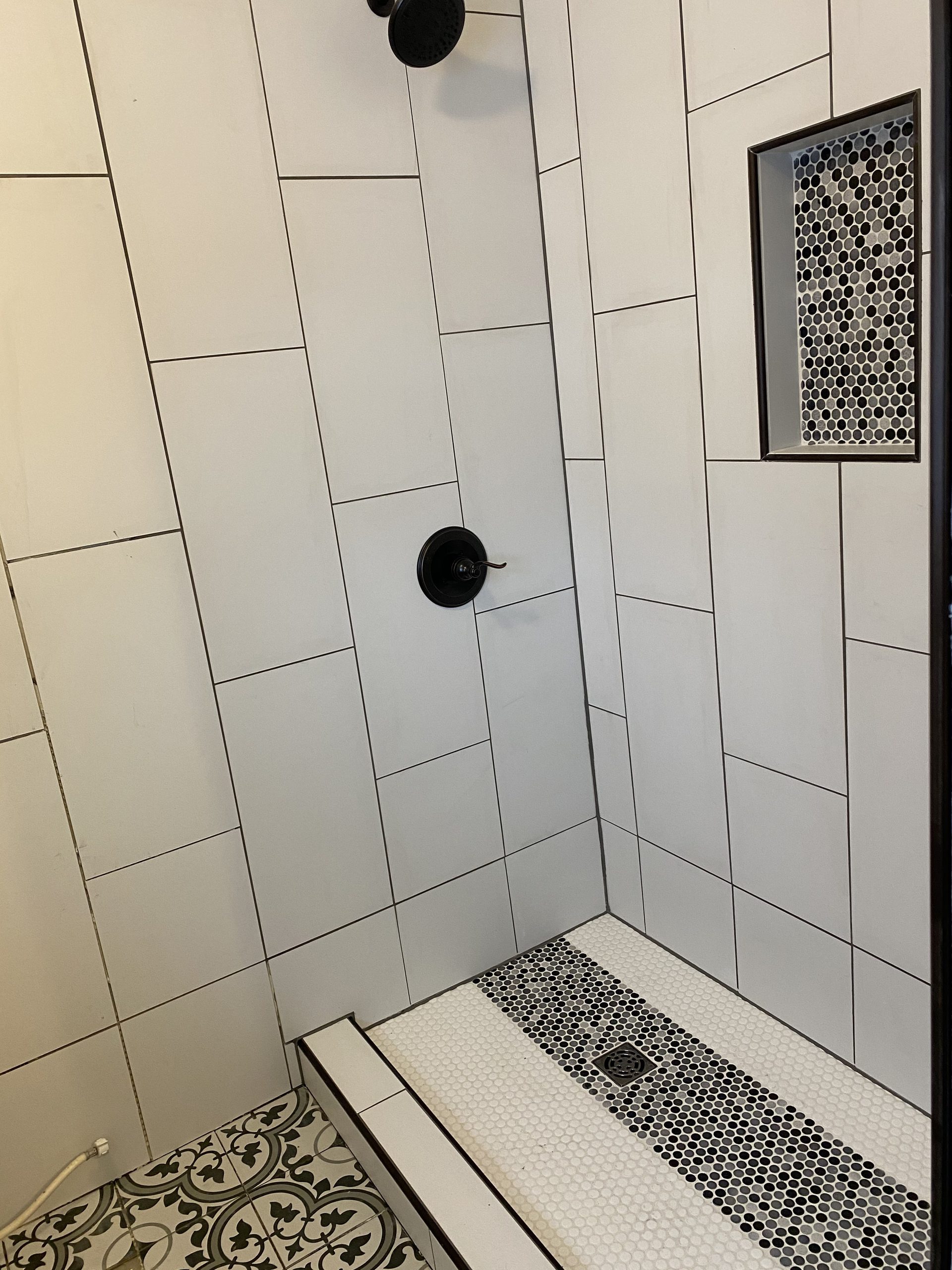 Completed tile shower with large white subway tiles, black grout lines, hexagonal mosaic floor in white and black, and matching hexagonal niche insert.