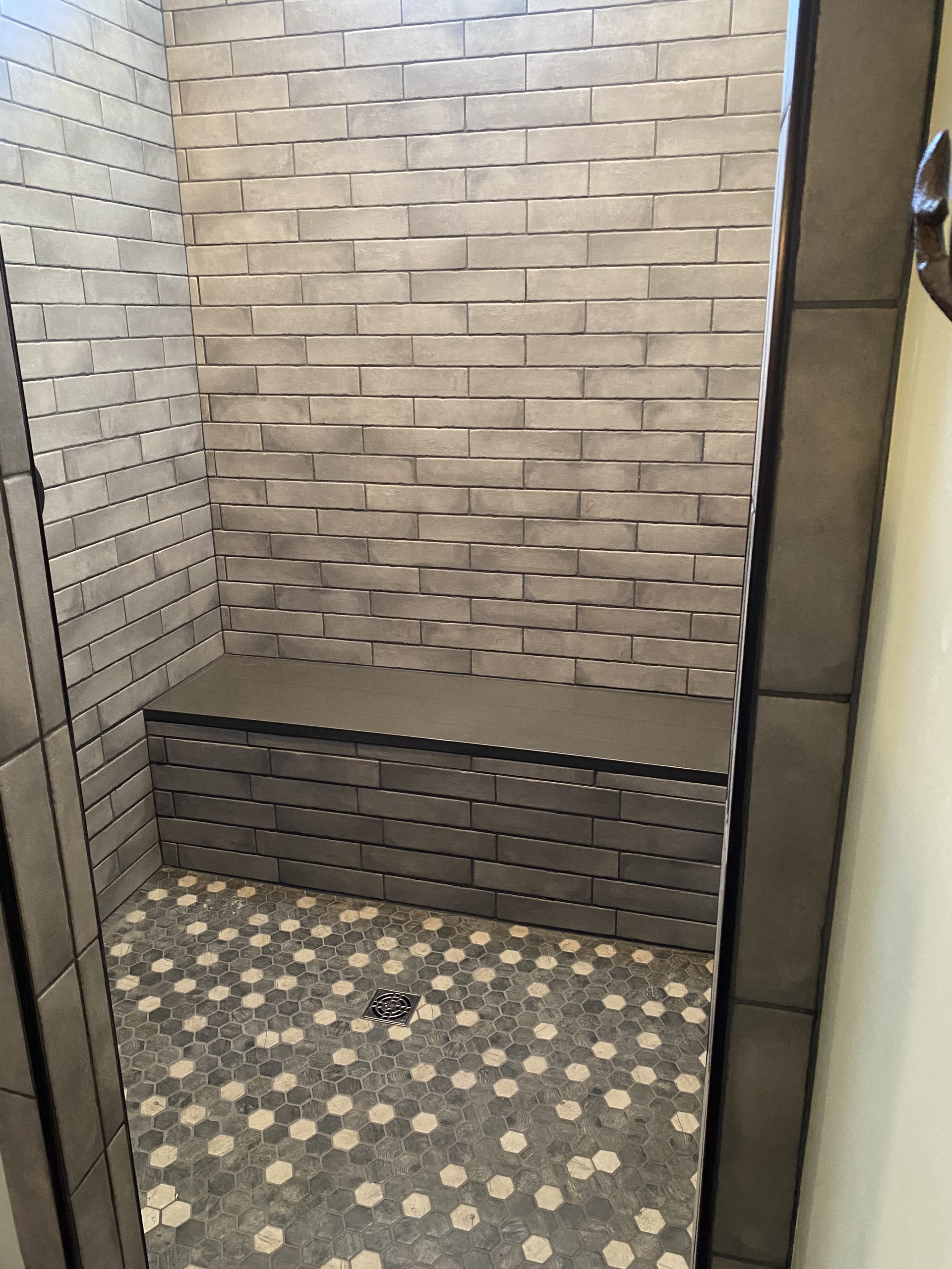 Finished tile shower with subway tile walls, penny tile floor in gray and cream, and built-in bench seat.