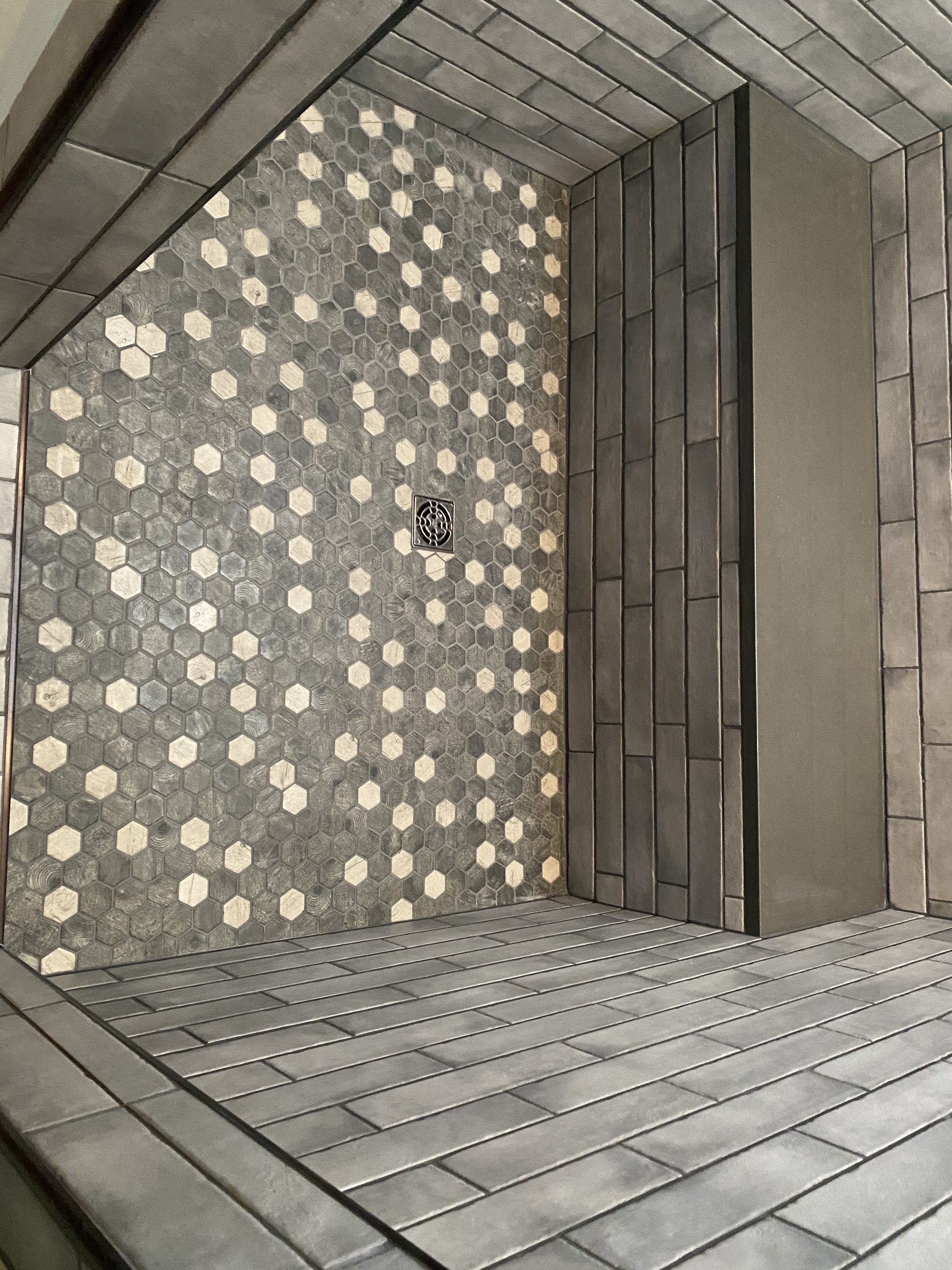 Completed tile shower with gray hexagonal mosaic tile wall and frameless glass enclosure