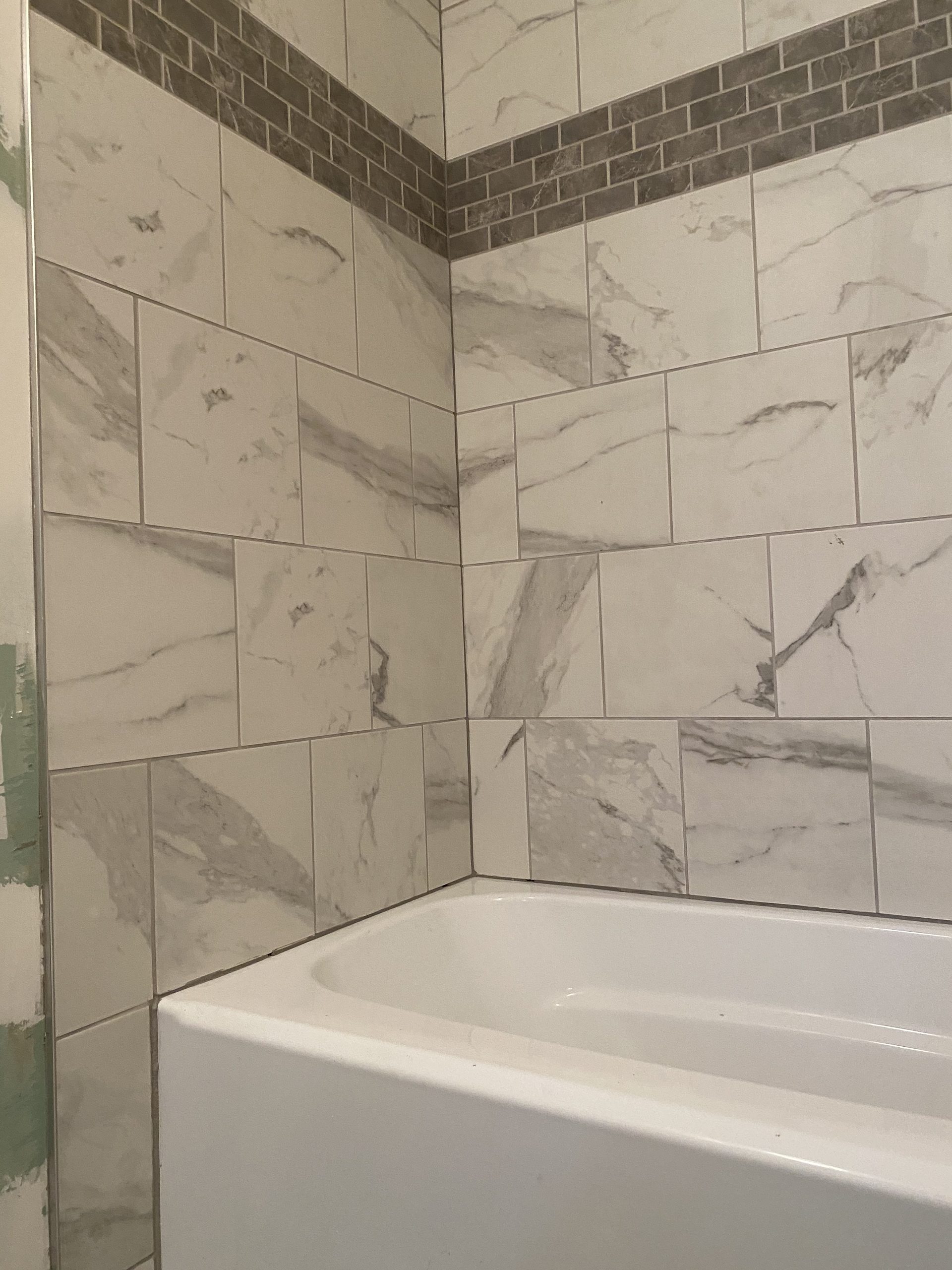 Marble tile shower surround with dark brick accent border above white bathtub