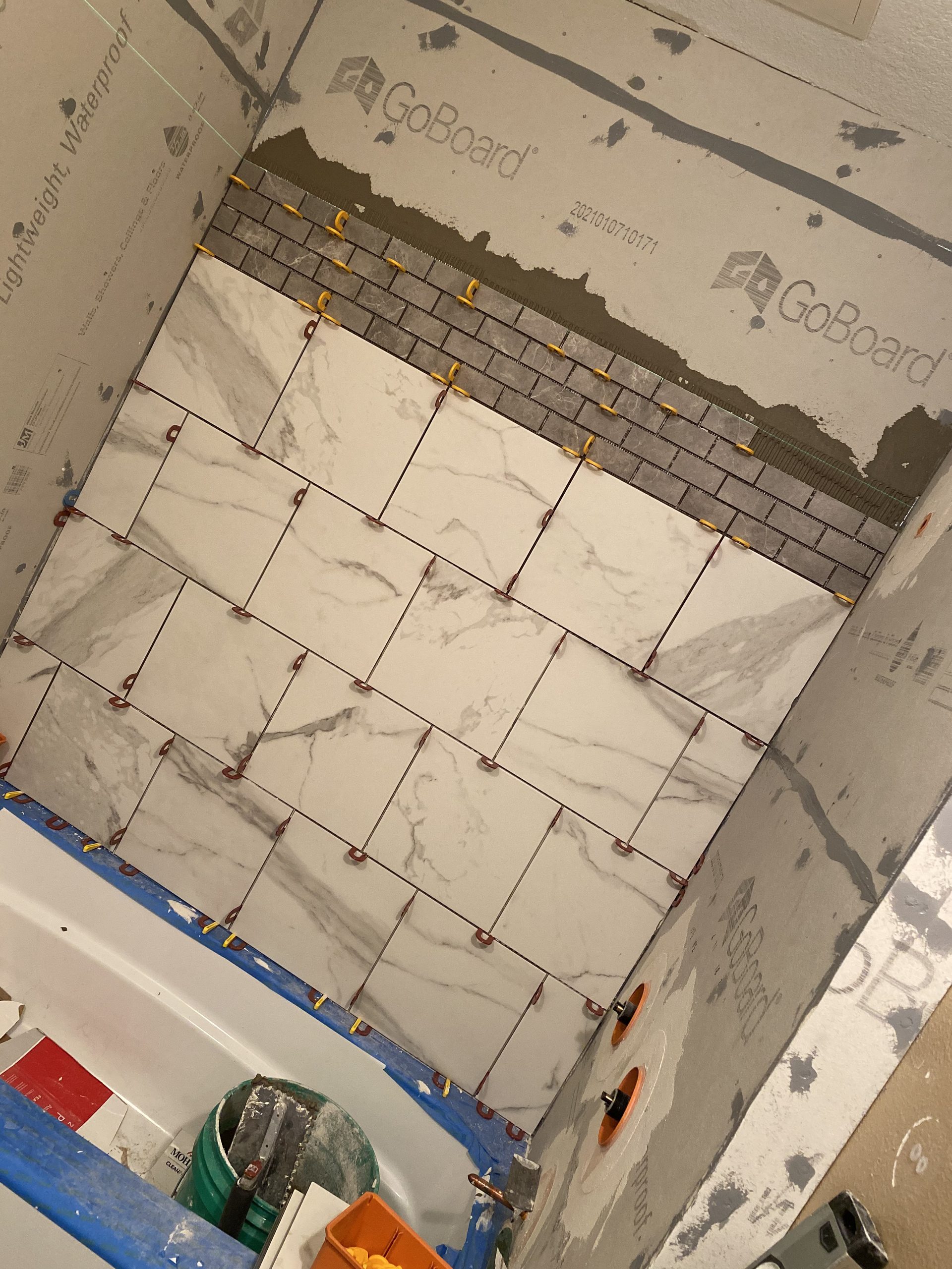 Marble tile installation in progress on a residential wall, showing organized tile layout with spacers and adhesive application.